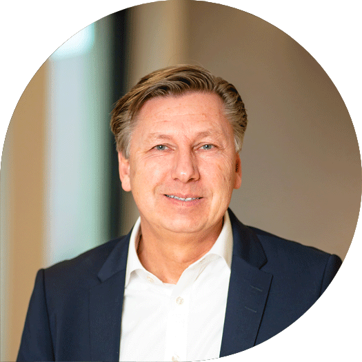 Porträt eines Mannes mit dunkelblondem Haar im dunklen Anzug und weißem Hemd, vor einem dezenten, modernen Hintergrund.