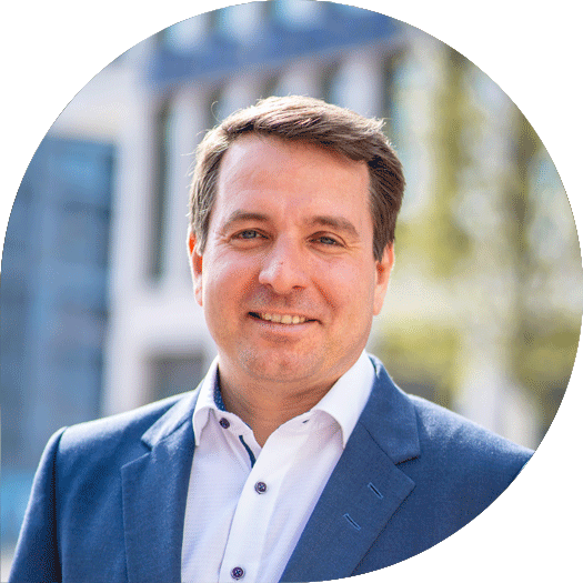 Porträt eines Mannes in dunkelblauem Anzug und weißem Hemd, lächelnd vor dem Hauptsitz der Heidelberger Volksbank.